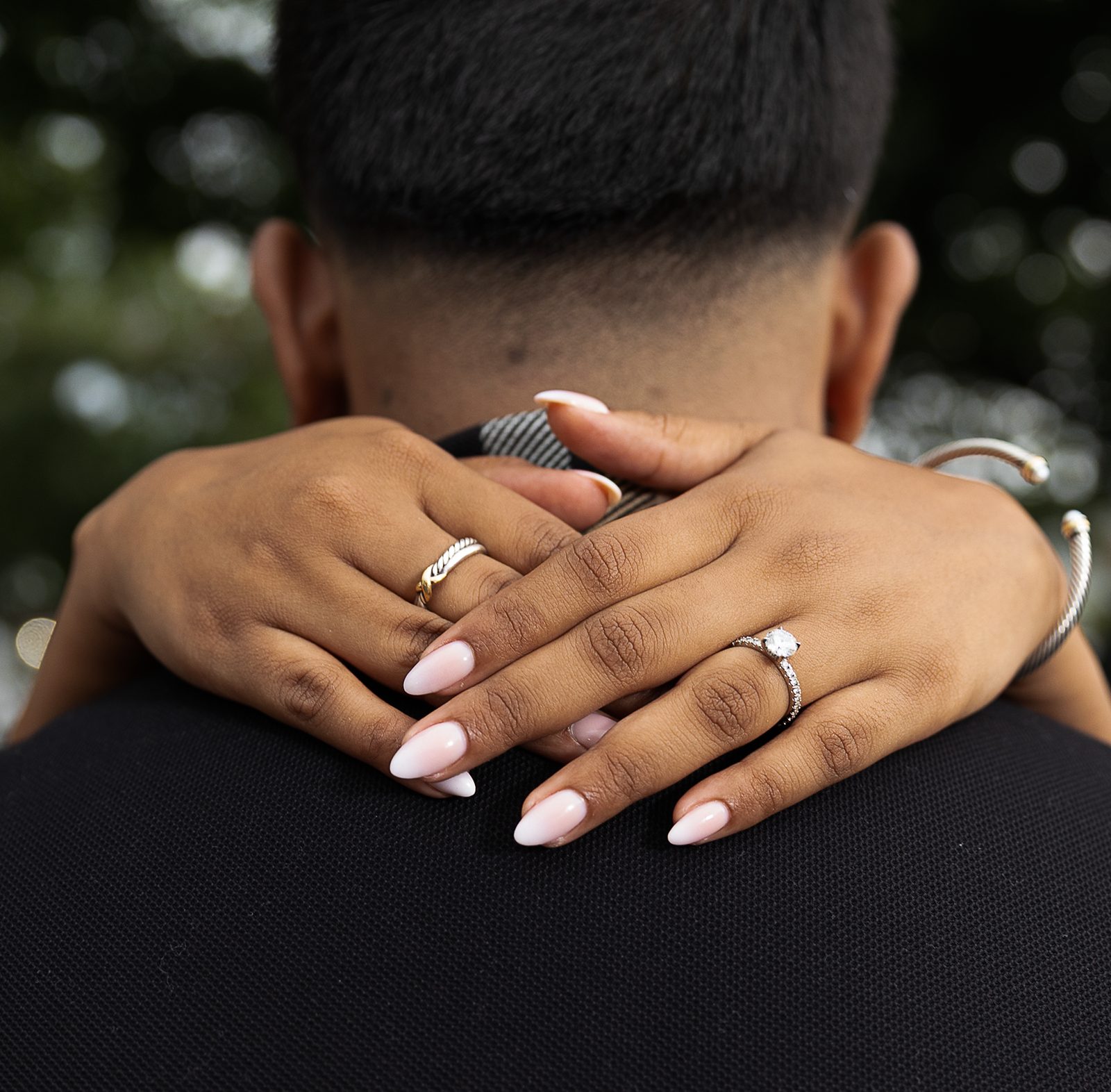 Hands with an engagement ring wrapped around a partner's neck
