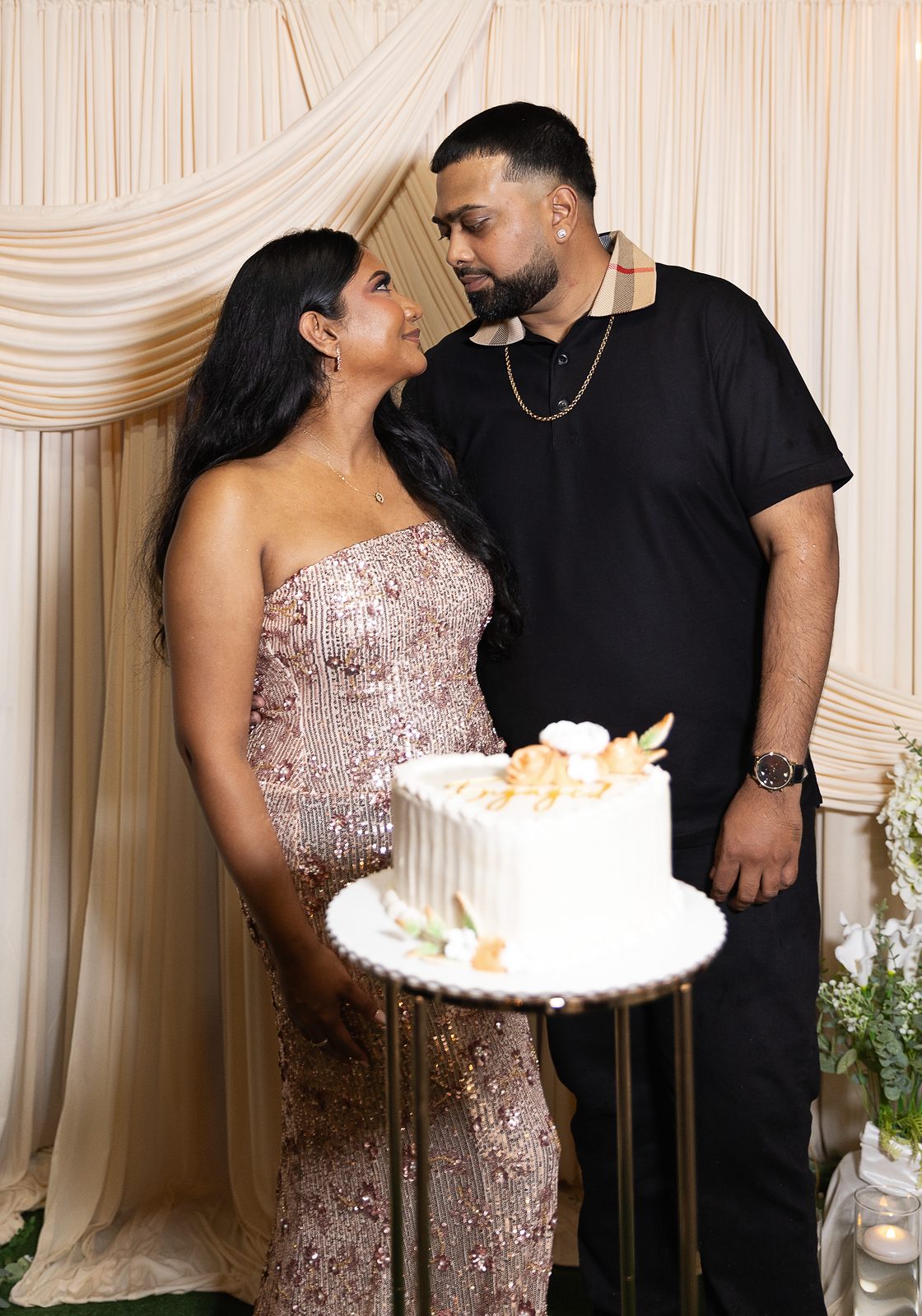 Engaged couple smiling at each other beside a cake