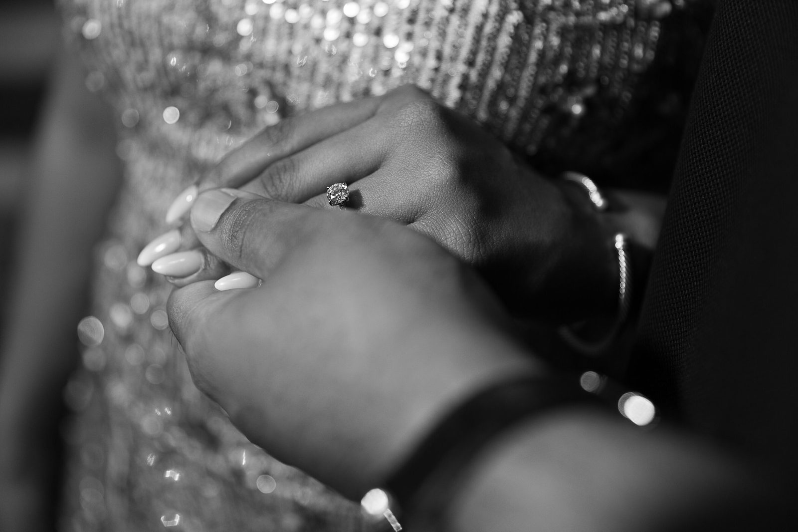 Black and white close-up of hands and an engagement ring