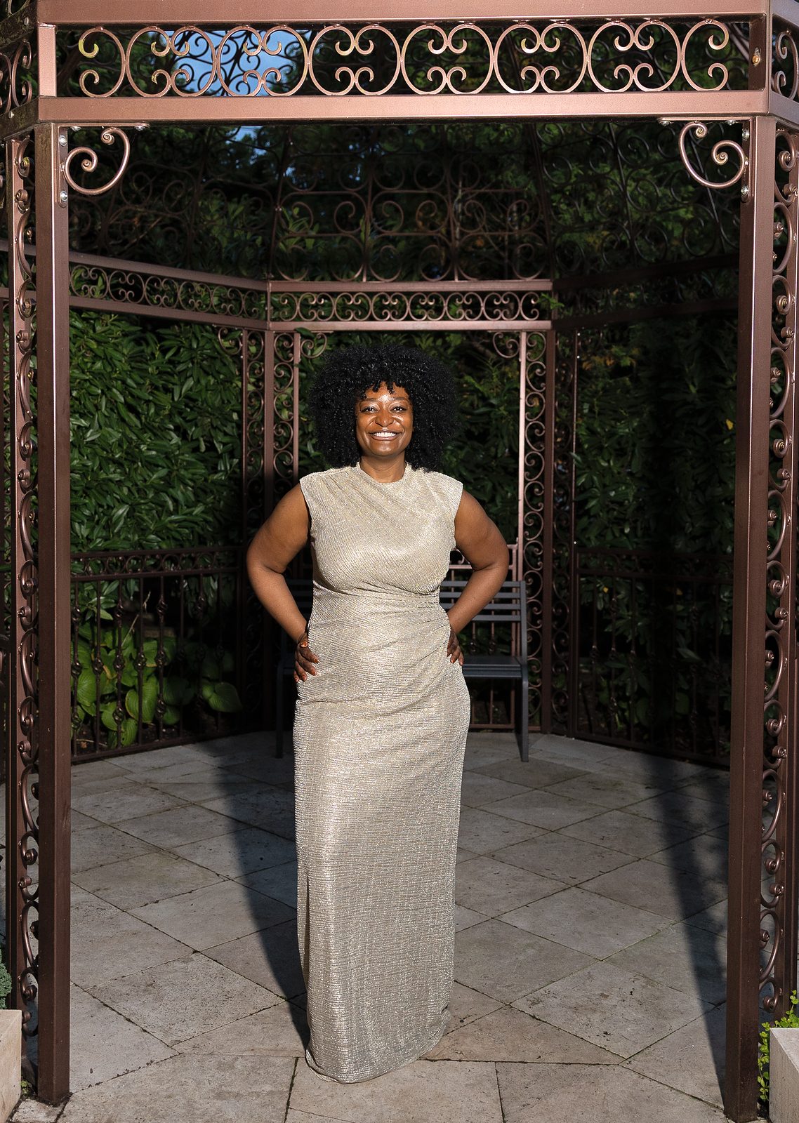 Woman in a gold gown posing under a garden gazebo